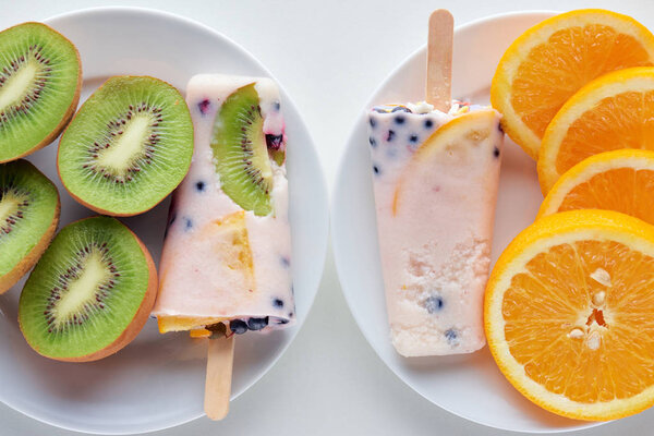 сверху вид на вкусные домашние фруктовые мороженое с ягодами и ломтиками апельсина и киви на тарелках на сером
