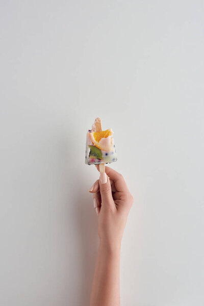 cropped shot of person holding fresh cold fruity popsicle on stick on grey 