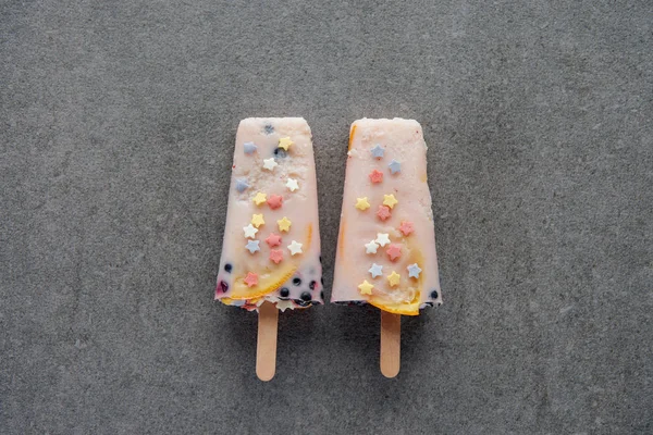 top view of sweet tasty popsicles on sticks on grey 