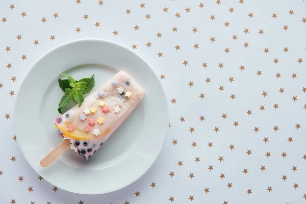 top view of delicious fruity popsicle with mint leaves on plate and beautiful golden stars on grey 