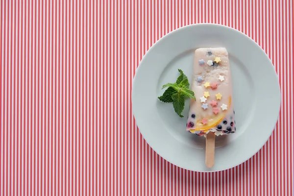 top view of delicious homemade popsicle with mint on plate on striped background