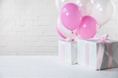 Presents on table with white and pink balloons on white brick wall background