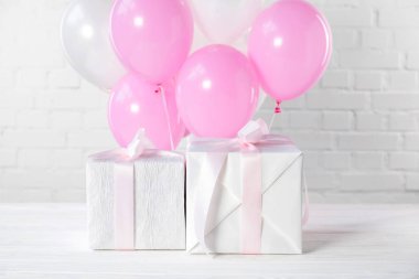 Gift boxes and decorative balloons on white brick wall background clipart
