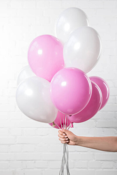 Female hand holding air balloons on white brick wall background