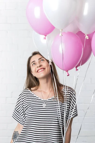 Woman looking up at pink and white balloons on white brick wall background