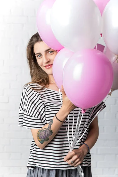 Happy girl holding bunch of balloons on white brick wall background