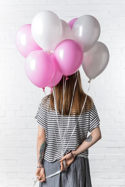 Rear view of woman with pink and white balloons on white brick wall background