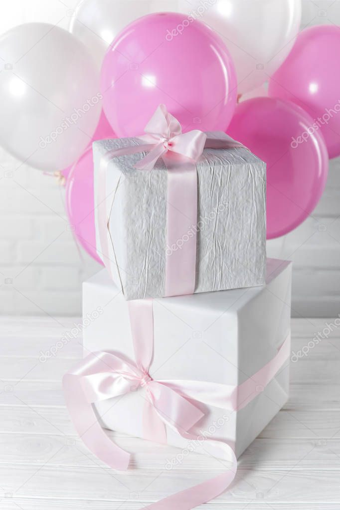 Stacked present boxes and bright balloons on white brick wall background
