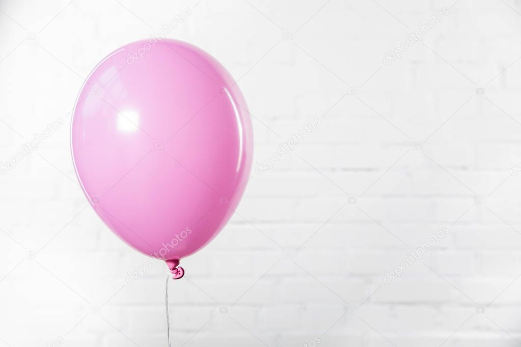 Single pink balloon on white brick wall background