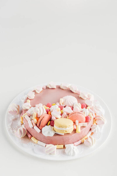 pink cake with marshmallows and macarons on white plate with copy space
