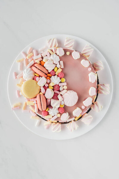 top view of pink birthday cake with marshmallows and macaroons on white plate