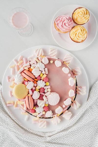 flat lay with pink birthday cake, marshmallows, cupcakes and milkshakes on table with tablecloth