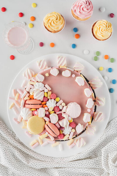 top view of birthday cake with marshmallows, candies and sweet cupcakes on table 