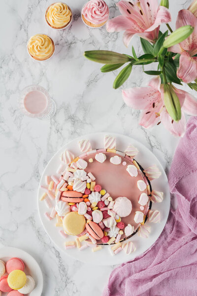 top view of sweet birthday cake with marshmallows and pink lily flowers on marble table 