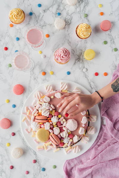cropped view of woman putting little candy on pink birthday cake
