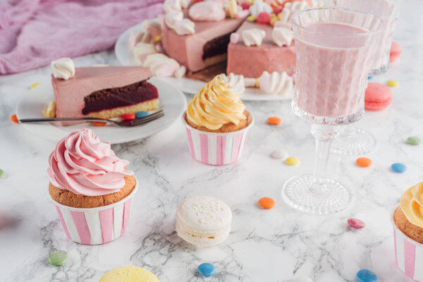 close up of pink cake, marshmallows, candies, sweet cupcakes and milkshake on marble table