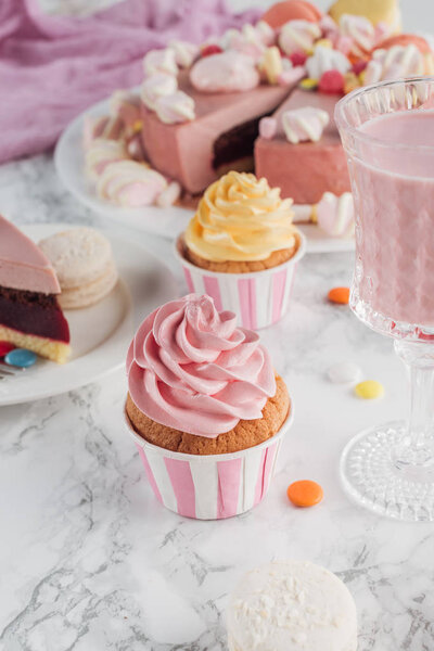 close up of birthday cupcakes, pink cake and milkshake in glass on marble table 