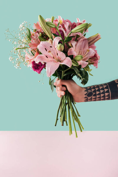 cropped view of tattooed male hand with bouquet of pink lily flowers