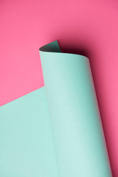 close-up view of rolled turquoise paper on pink background 