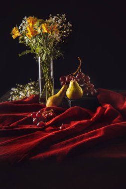 still life with ripe fruits and flowers in vase on red drapery on black clipart