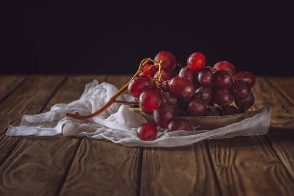 close-up shot of ripe grapes on cheesecloth and on rustic wooden table on black