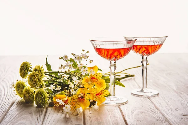 close-up shot of glasses of wine with field flowers bouquet on wooden table on white