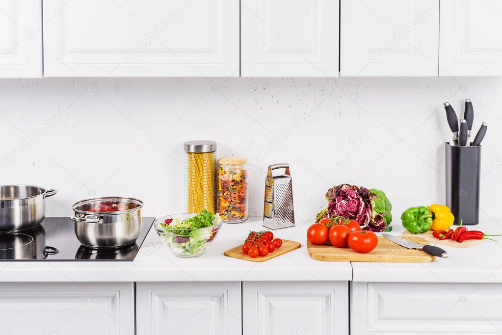 ripe vegetables on cutting boards, pans on electric stove in light kitchen