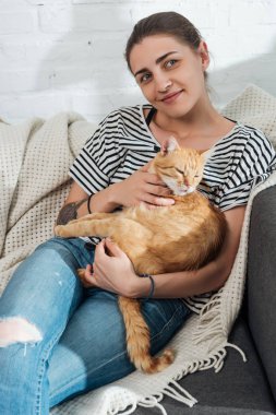 güzel genç kadın holding kırmızı kedi gülümseyen ve kanepede oturan