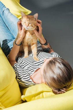 Kızın sarı koltukta yalan sırasında şirin kırmızı kedi ile oynarken yüksek açılı görünüş