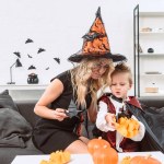 Mother and little son in halloween costumes with black paper bats on sofa at home