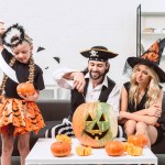 Family in halloween costumes on sofa at coffee table with pumpkins at home