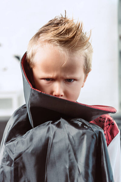 portrait of little boy in vampire halloween costume looking at camera at home