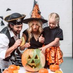 Portrait of parents and little daughter in halloween costumes looking into pumpkin together at home