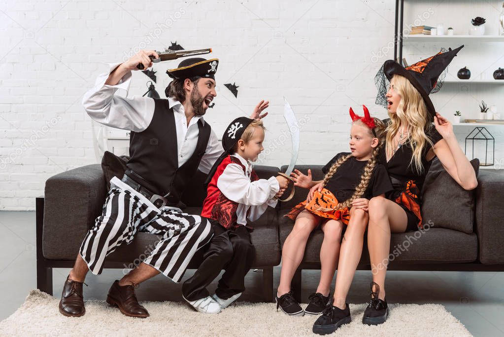 father and son in pirates costumes scaring mother and daughter on sofa at home