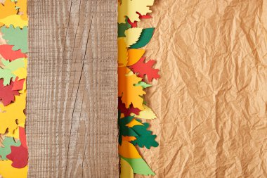 top view of wooden plank and colorful paper leaves arrangement on crumpled paper backdrop clipart