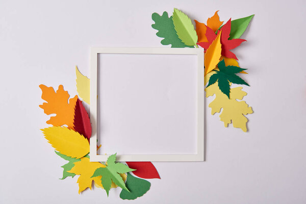flat lay with handcrafted paper leaves and empty frame on white tabletop