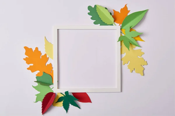 flat lay with handcrafted paper leaves and empty frame on white tabletop