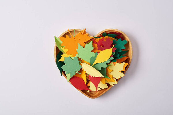 top view of wooden heart shaped box and colorful handcrafted leaves on white surface