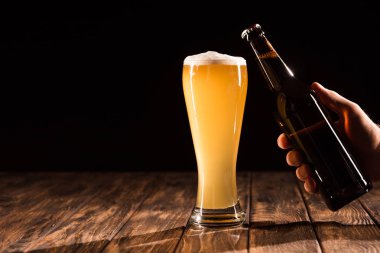 partial view of man clinking beer bottle with mug of fresh beer at wooden table  clipart