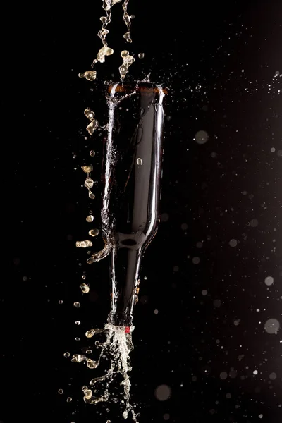 selective focus of beer pouring on bottle upside down with splashes around isolated on black background
