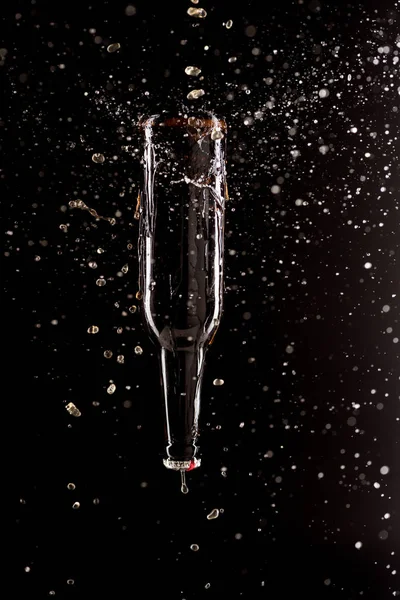 beer bottle upside down with splashes around isolated on black background