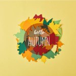 Vlakke leggen met kleurrijke papercrafted gebladerte met "Hallo herfst" belettering in cirkel op gele achtergrond