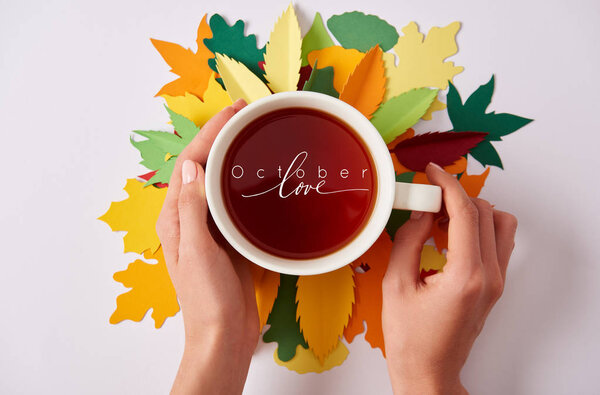 partial view of woman holding cup of hot tea with "october love" inspiration on colorful papercrafted leaves