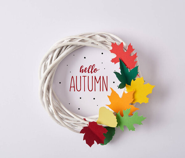 top view of handmade wreath with colorful paper foliage and "hello autumn" lettering on white backdrop