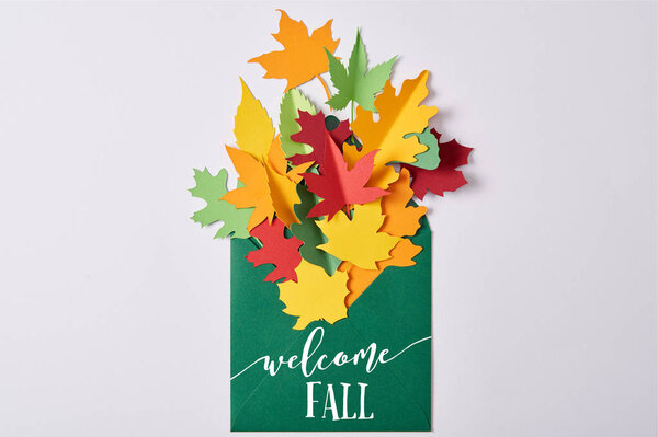 top view of colorful handcrafted paper leaves in green envelope with "welcome fall" lettering on white background