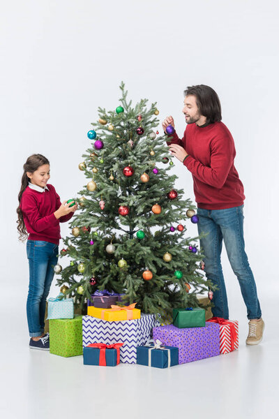 Happy father looking at daughter decorating christmas tree with glass balls isolated on white