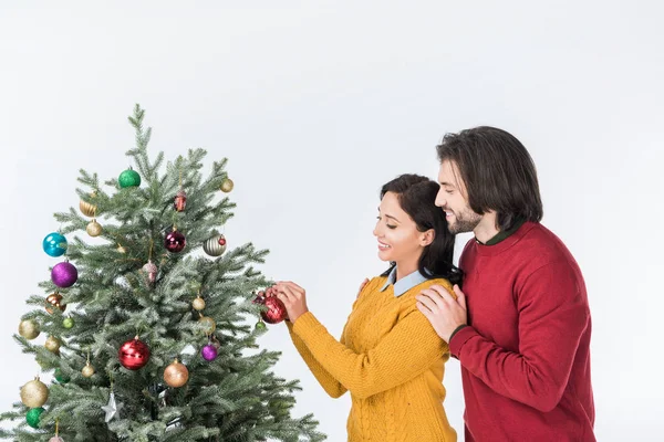 smiling man hugging woman decorating christmas tree with presents isolated on white