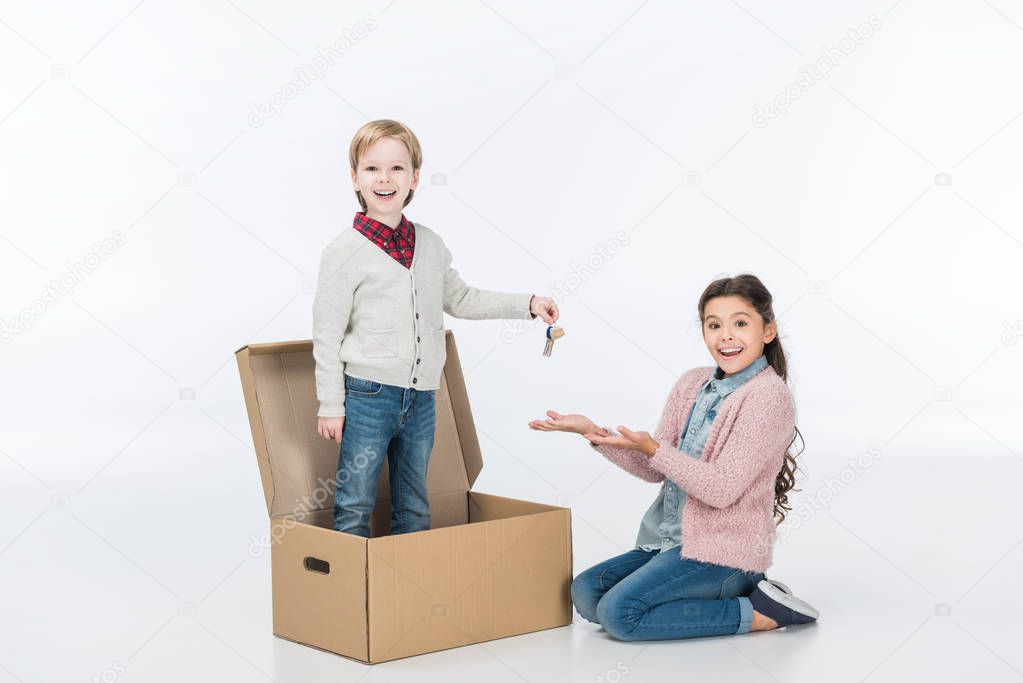 Little boy giving key from new house to surprised sister ready to move into new house isolated on white 