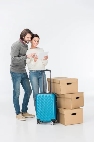 スーツケースと段ボール箱が白で隔離の近くに立ってデジタル タブレットを使用して幸せなカップル — ストック写真