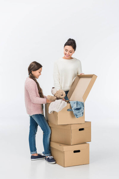 улыбающиеся мать и дочь с картонными коробками переезда в новый дом изолированы на белом
 